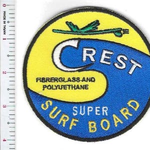 May include: A circular embroidered patch featuring a yellow and blue wave design with the text CREST, FIBERGLASS AND POLYUETHANE, and SUPER SURF BOARD. A green surfboard icon sits at the top. A ruler shows the patch is approximately 3.5 inches wide.