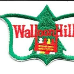 Könnte beinhalten: Gestickter Aufnäher mit dem Text "Walloon Hills" in Rot, vor einem grünen schildförmigen Design. Der Aufnäher zeigt einen stilisierten grünen Baum und ein rotes Gebäude. Der Aufnäher ist wahrscheinlich ein Souvenir oder ein Emblem.