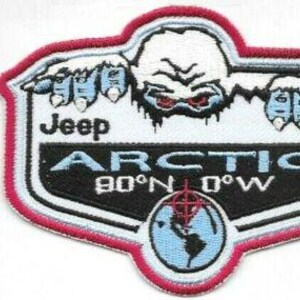 Op de afbeelding: Geborduurde patch met een witte yeti met rode ogen en blauwe handen, boven de tekst "Jeep ARCTIC 90°N 0°W". De patch heeft een rood, wit en zwart kleurenschema met een wereldbol-afbeelding.