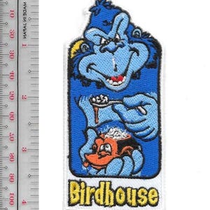 Peut inclure: Un écusson brodé rectangulaire représentant un personnage bleu de dessin animé tenant une cuillère au-dessus d'une créature orange, avec le texte Birdhouse en jaune en bas. Une règle à côté montre une longueur d'environ 10 cm.