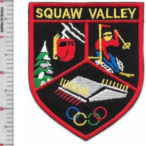 Puede incluir: Parche bordado con las palabras "SQUAW VALLEY" en amarillo. El parche presenta un esquiador, un telesilla, un edificio, un árbol y los anillos olímpicos en rojo, blanco, azul, verde y amarillo. El parche es negro con un borde rojo.