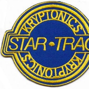 May include: A blue and yellow embroidered patch with the words "KRYPTONICS" and "STAR-TRAC". The patch is circular with a rectangular border. The text is in yellow.