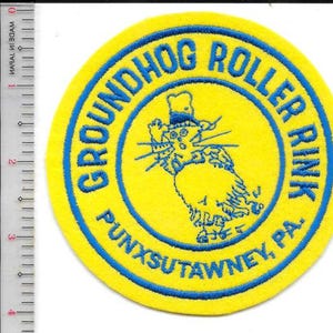 May include: A round yellow patch with blue text and a cartoon groundhog wearing a hat. The text reads "GROUNDHOG ROLLER RINK" and "PUNXSUTAWNEY, PA." in a circular pattern. The groundhog is in the center.