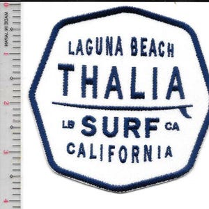 Puede incluir: Parche blanco y azul marino con el texto "LAGUNA BEACH THALIA SURF CALIFORNIA". El parche tiene un borde azul marino y un gráfico de tabla de surf. El parche mide aproximadamente 7.6 cm de ancho.