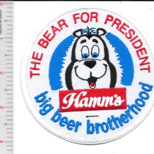 May include: A circular patch with the text "THE BEAR FOR PRESIDENT" in red, and "big beer brotherhood" in blue. The patch features a cartoon bear with blue eyes and a red tongue, and the Hamm's logo.