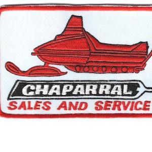 Op de afbeelding: Geborduurde patch met een rood sneeuwscooterontwerp op een witte achtergrond, omlijst door een rode rand. De tekst "CHAPARRAL SALES AND SERVICE" wordt in zwart en rood weergegeven.