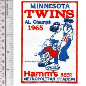 May include: A rectangular patch featuring the Minnesota Twins logo with text that reads "MINNESOTA TWINS AL Champs 1965." The patch includes cartoon bear figures in baseball uniforms. The bottom text reads "Hamm's BEER METROPOLITAN STADIUM."