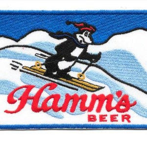 May include: Embroidered patch featuring a cartoon bear skiing down a snowy mountain. The bear wears a hat and scarf. The patch has a blue border and the words "Hamm's BEER" in red.