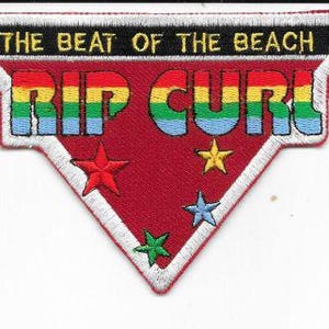 May include: Embroidered patch with the text "THE BEAT OF THE BEACH" and "RIP CURL" in rainbow colours. The patch is red with white trim and features star accents in red, yellow, green, and blue.