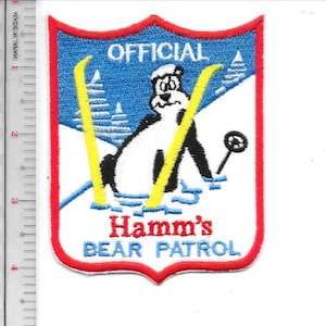 May include: Embroidered patch with a shield design. The patch features a cartoon bear skiing with yellow skis, the text "OFFICIAL" at the top, and "Hamm's BEAR PATROL" at the bottom. The border is red, with blue and white accents.