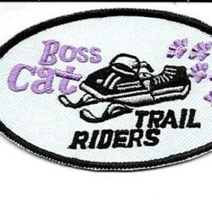 May include: Oval patch with the text "Boss Cat Trail Riders" in black and purple. The patch features a snowmobile design and paw prints. The border is black.
