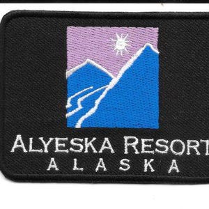 May include: Black embroidered patch featuring the words "ALYESKA RESORT ALASKA" in white. The patch has a rectangular shape with a mountain scene in the center, with blue mountains, a purple sky, and a white sun.