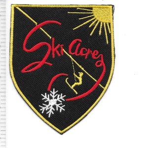May include: A black patch with a yellow border, featuring the red text "Ski Acres" in a script font. A yellow sun and skier graphic are also present. A white snowflake is at the bottom. The patch is shield-shaped.