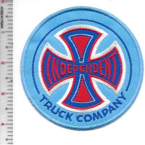 May include: A round, light blue patch with a red and white cross design. The word "INDEPENDENT" is in red, and "TRUCK COMPANY" is written in blue around the edge. The patch is approximately 4 inches in diameter.