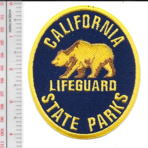 May include: A circular patch with a yellow border and text that reads "CALIFORNIA LIFEGUARD STATE PARKS." The patch features a yellow bear on a navy blue background. The patch is approximately 7.6 cm in diameter.