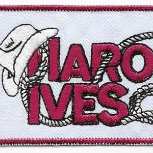 May include: Embroidered patch with the text "HAROLD IVES" in maroon, encircled by a rope design, and a white cowboy hat. The patch has a white background and a maroon border.