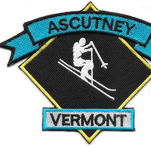 Könnte beinhalten: Gestickter Aufnäher mit einem weißen Skifahrer auf einem schwarzen Diamanten, mit dem Text "ASCUTNEY" in einem blauen Banner darüber und "VERMONT" in einem blauen Rechteck darunter. Der Aufnäher hat einen gelben Rand.