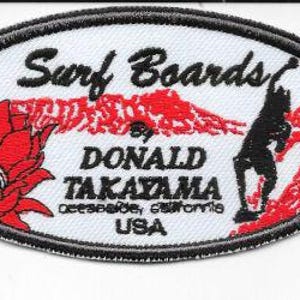 May include: Oval patch with the text "Surf Boards" and "DONALD TAKAYAMA" in black. The patch features a red mountain range, a surfer silhouette, and a red flower. The text "Oceanside, California USA" is also included.