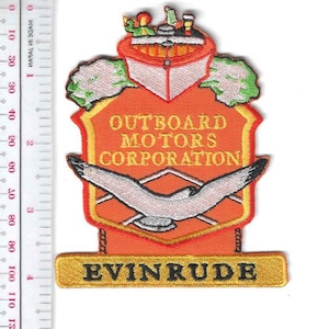 May include: Embroidered patch featuring the text "OUTBOARD MOTORS CORPORATION" and "EVINRUDE" on an orange shield with a seagull design. The patch has a boat graphic at the top and is approximately 4 inches in height.