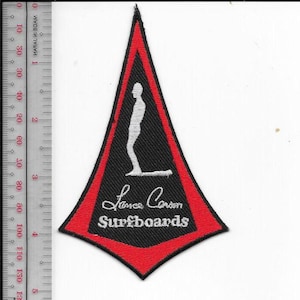 May include: A black and red patch with a white silhouette of a person surfing. The patch has the text "Lance Carson Surfboards" in white script. The patch is in the shape of a triangle.