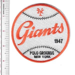 Może przedstawiać: Okrągła naszywka baseballowa z białym tłem i pomarańczową obwódką. Słowo "Giants" jest w pomarańczowym skrypcie, z "1947" poniżej. Naszywka zawiera również "POLO GROUNDS NEW YORK".