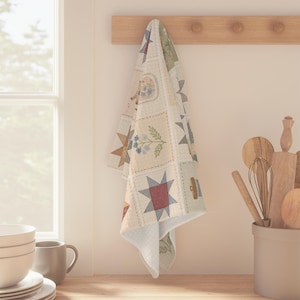 May include: A cream-colored kitchen towel with a patchwork design featuring stars, floral patterns, and other geometric shapes. The towel is hanging from a wooden rack with pegs, showcasing a rustic, country-style aesthetic.