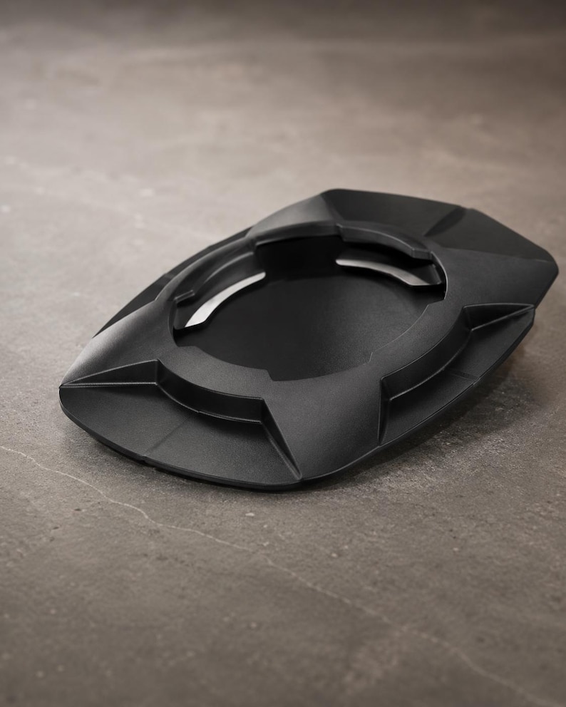 May include: A black ashtray with a geometric design. The ashtray has a central circular depression and several angled rests for cigarettes. The overall shape is a flattened oval with sharp, angular edges. The ashtray is made of a matte black material.