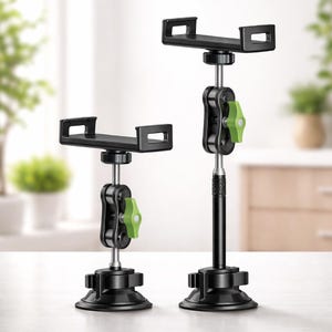 Könnte beinhalten: Zwei schwarze Telefonhalter mit verstellbaren Armen und grünen Knöpfen. Die Halterungen haben einen Saugnapf-Sockel für sicheren Halt. Einer ist kürzer als der andere und bietet verschiedene Höhenoptionen. Der Hintergrund ist unscharf.