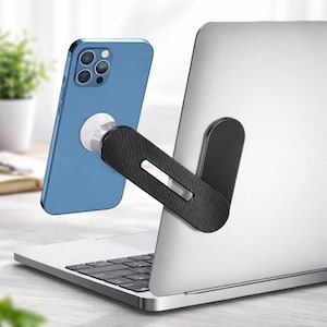 May include: A blue smartphone is magnetically attached to a black and silver laptop stand. The stand is connected to the back of a silver laptop. The phone is blue and has a silver magnetic attachment. The stand has a carbon fibre texture.