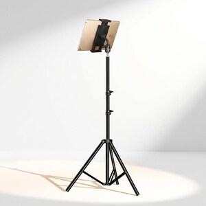May include: A gold tablet mounted on a black adjustable tripod stand. The stand features a three-legged base with central support struts and two locking knobs on the vertical pole to adjust height. The tablet is held by a black plastic clamp.