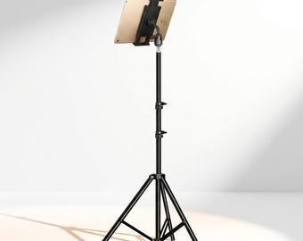 May include: A gold tablet mounted on a black adjustable tripod stand. The stand features a three-legged base with central support struts and two locking knobs on the vertical pole to adjust height. The tablet is held by a black plastic clamp.