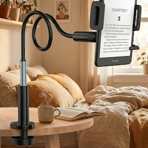 Könnte beinhalten: Ein schwarzer, verstellbarer Tablet-Halter mit flexiblem Arm, an einem Holztisch befestigt. Ein E-Reader zeigt "CHAPTER 1" und Text an. Eine Tasse und ein offenes Buch liegen daneben. Der Halter ist für freihändiges Lesen konzipiert.