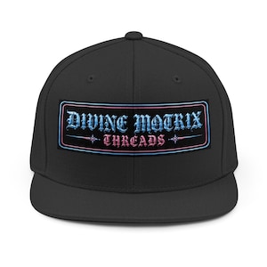 May include: A black snapback cap featuring a rectangular patch on the front. The patch displays the text "DIVINE MATRIX" in a light blue gothic font above the word "THREADS" in a pink gothic font, all enclosed by a thin blue and pink border.