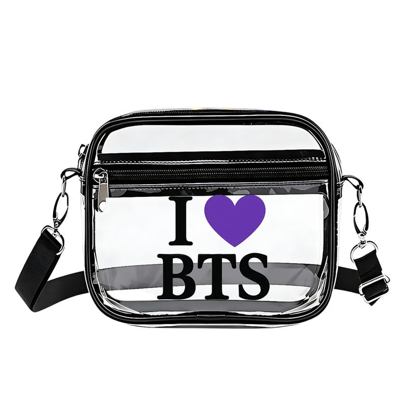 May include: Clear crossbody bag with black trim and a black adjustable strap. The bag features the text "I &hearts; BTS" with a purple heart. The bag has a zippered top and silver hardware.