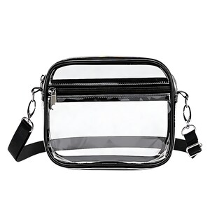 May include: A clear, rectangular crossbody bag with a black trim and zipper. The bag has a black adjustable shoulder strap and silver-tone hardware. The transparent design allows visibility of the contents.