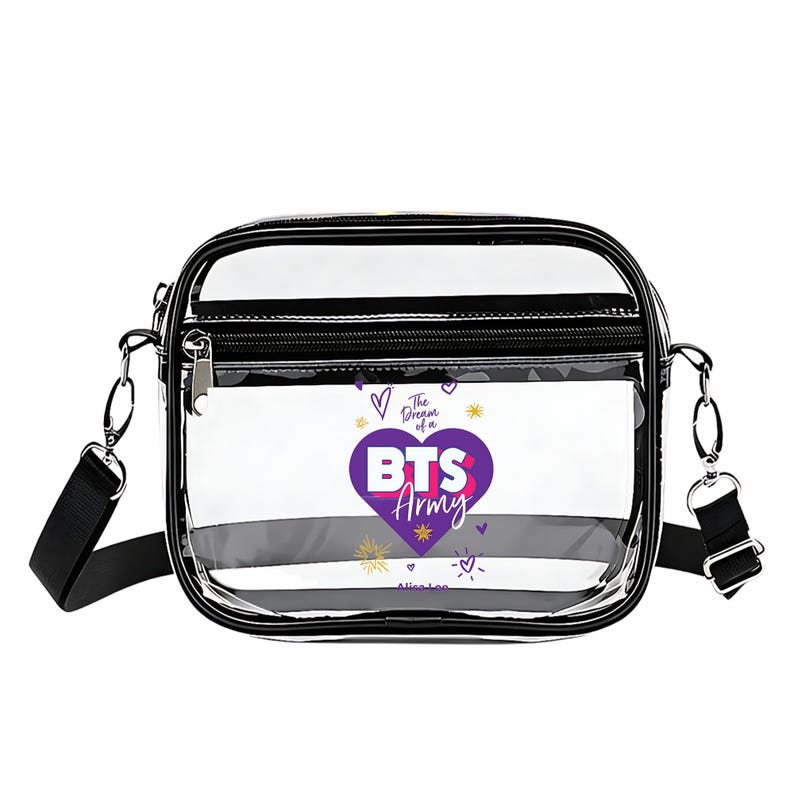 May include: Clear crossbody bag with black trim and a black adjustable strap. The bag features a purple heart with the text "BTS Army" and the phrase "The Dream of a". The bag has a zippered top and a small front pocket.