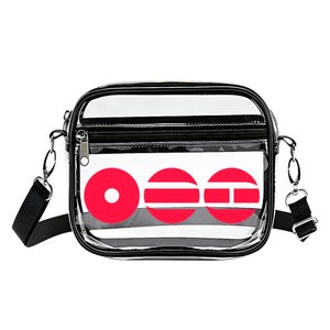 May include: Clear crossbody bag with a black strap and trim. The bag features a white panel with three red circular designs. A zippered pocket is visible on the front.