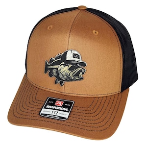 May include: A brown and black trucker hat with a fish graphic wearing sunglasses and a hat. The hat has a curved brim and an adjustable strap. The Richardson brand logo is visible on the front.