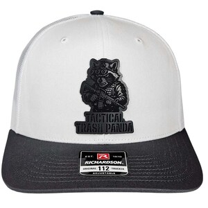 May include: White and charcoal gray trucker hat with a patch featuring a raccoon wearing goggles and holding a rifle. The patch reads "TACTICAL TRASH PANDA". The hat has a curved brim and an adjustable strap.