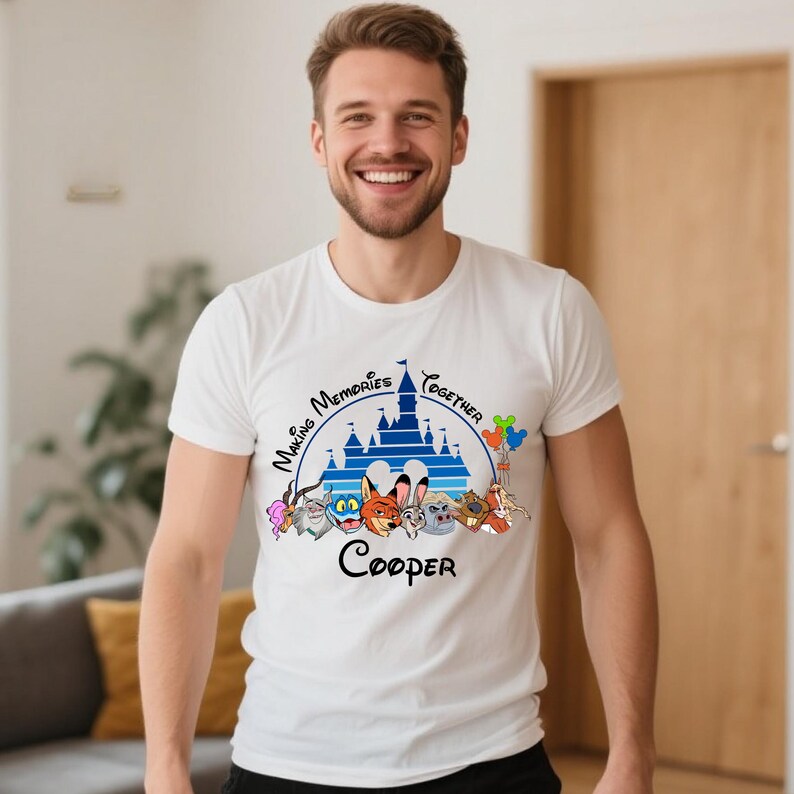 Puede incluir: Camiseta blanca con un gr&aacute;fico colorido que presenta un castillo azul, personajes de dibujos animados y el texto "Making Memories Together" y "Cooper". El dise&ntilde;o incluye una variedad de animales de dibujos animados y globos coloridos.
