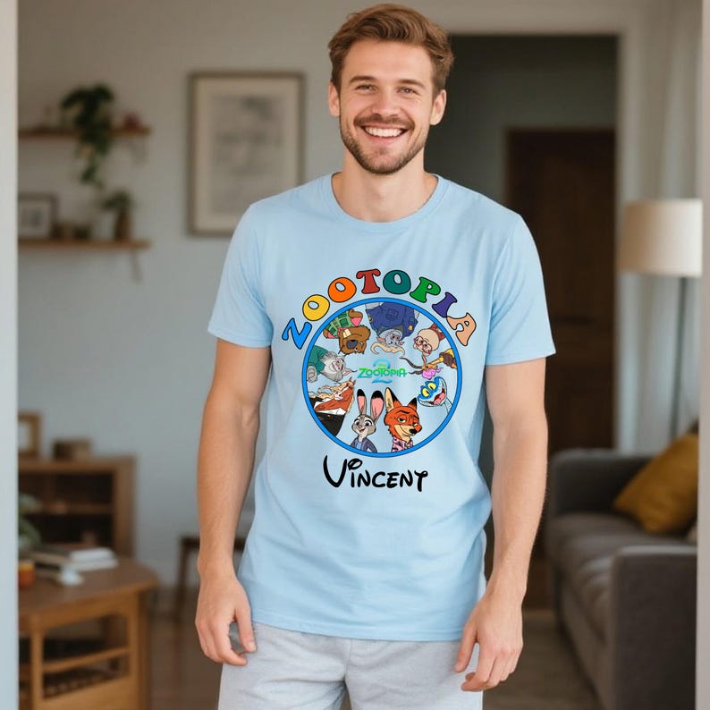 May include: Light blue t-shirt featuring the word "ZOOTOPIA" in colorful letters, with cartoon characters in a circular design. The name "Vincent" is printed below the design. The shirt is short-sleeved.
