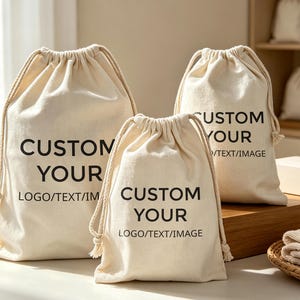 Può includere: Tre sacchetti con coulisse color bianco sporco di varie dimensioni realizzati in tessuto intrecciato. Ogni sacchetto presenta il testo stampato in nero CUSTOM YOUR LOGO/TEXT/IMAGE sul davanti. I sacchetti hanno spessi cordini intrecciati.