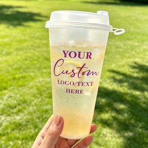 May include: A frosted plastic cold cup with a white lid, filled with a light yellow carbonated beverage and a lemon slice. The cup features purple text that reads YOUR Custom LOGO/TEXT HERE printed on the front surface of the container.