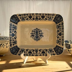 May include: A rectangular ceramic serving platter with a cream-colored base and a dark blue intricate floral and scrollwork pattern along the border and a matching symmetrical decorative motif centered on the flat surface of the platter.