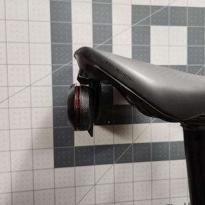 Pode incluir: Um selim de bicicleta preto com uma luz traseira vermelha e preta presa. O selim &eacute; rotulado "Body Geometry". A luz &eacute; redonda e tem uma borda texturizada. O espig&atilde;o do selim &eacute; preto.