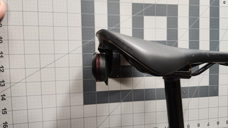 Pode incluir: Um selim de bicicleta preto com uma luz traseira vermelha e preta presa. O selim &eacute; rotulado "Body Geometry". A luz &eacute; redonda e tem uma borda texturizada. O espig&atilde;o do selim &eacute; preto.