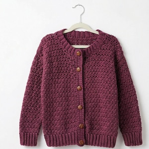 May include: A burgundy crochet cardigan with a round neckline and long sleeves, hanging on a white hanger. The button-down sweater features wooden buttons and ribbed cuffs and hem. The open weave design is visible throughout the garment.