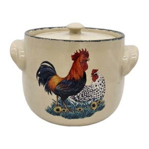 May include: A cream-colored ceramic crock with a matching lid and two side handles. The front features a colorful illustration of a rooster and a hen standing in green grass with yellow sunflowers, finished with a dark, distressed rim detail.