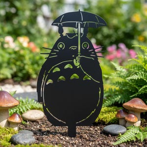 May include: A black metal garden stake featuring a silhouette of a large, round creature with pointed ears, whiskers, and a patterned belly, holding an open umbrella above its head. The design is cut from a flat sheet of dark metal.