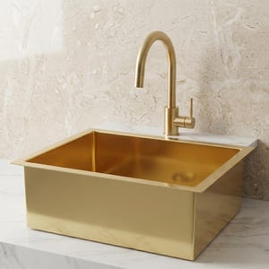 Könnte beinhalten: Ein rechteckiges, goldfarbenes Küchenbecken mit einer passenden goldenen Armatur. Das Waschbecken ist in eine weiße Arbeitsplatte eingelassen. Die Armatur hat einen gebogenen Auslauf und einen Einhebelgriff. Der Hintergrund ist eine hellbeige marmorartige Wand.